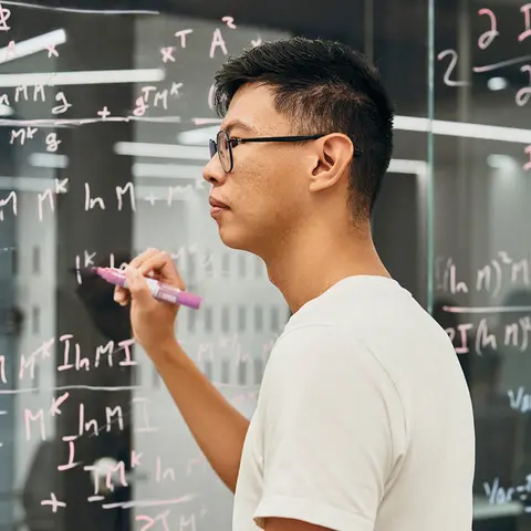 A man writing algorithms on a glass wall.